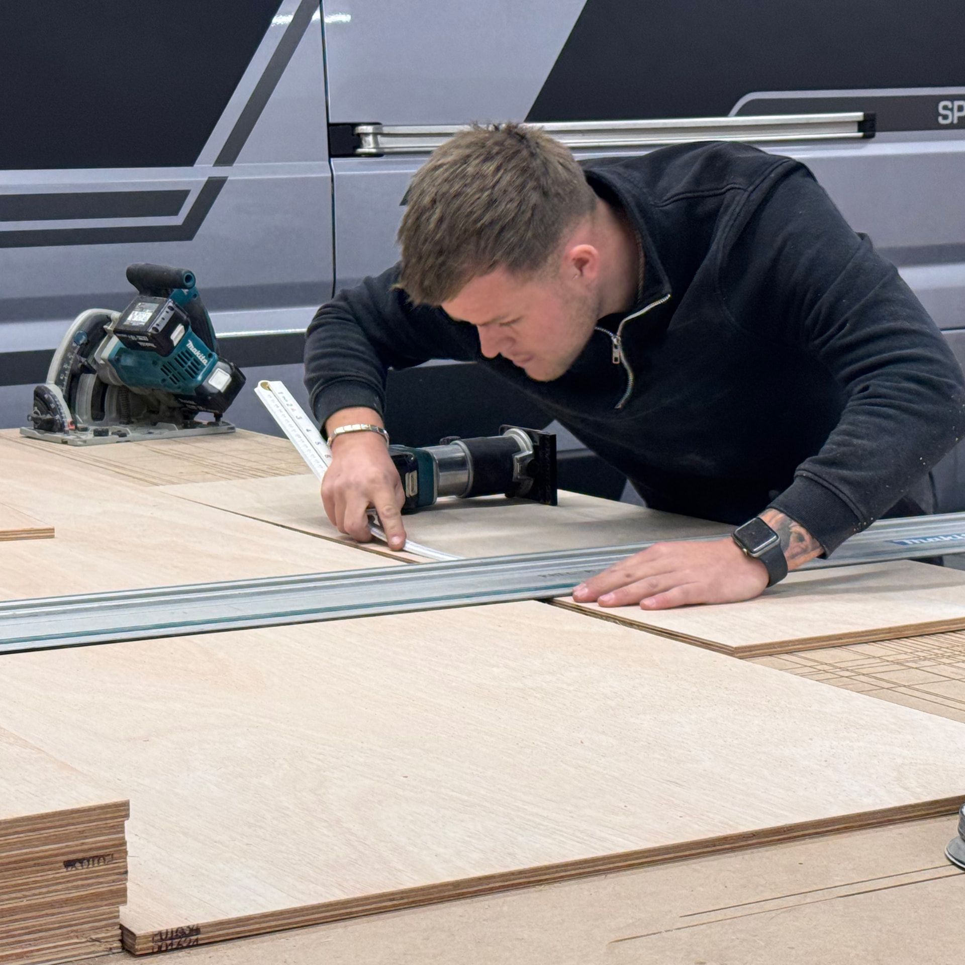 Van fitter cutting plywood panels at the ProCraft workshop in Dingwall with vans in the background
